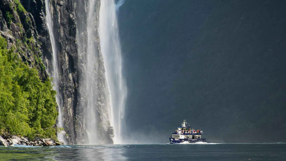 Hybrid-electric catamaran on a Geiranger fjord cruise from Ålesund passing steep UNESCO fjord walls in Norway